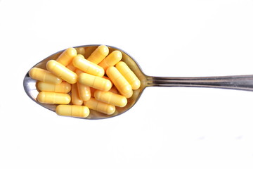 Full steel spoon of yellow pills in capsule on white background. Isolated. Top view