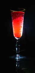 illuminated patterned glass of red wine with gold shadow with reflection on dark background