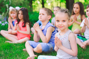 A large group of children engaged in yoga in the Park sitting on the grass.