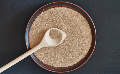 Amaranth seeds on a brown plate on a black background close-up.