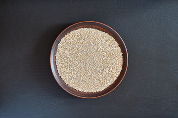 Seeds, white quinoa on a brown plate on a black background close-up.