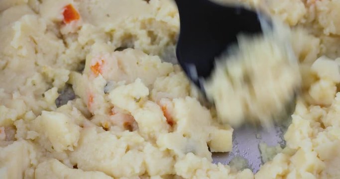 Close video of stirring canned potato soup in a pan with a black spoon while heating.