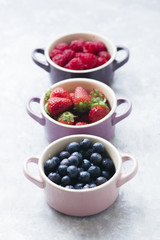 Summer fruit background, top view of berries inside ceramic colored cocotte, blueberries, strawberries, raspberries, flat lay, blue table. Detox and healthy food concept.