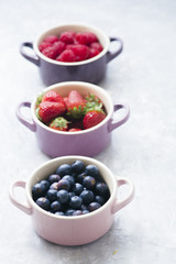 Summer fruit background, top view of berries inside ceramic colored cocotte, blueberries, strawberries, raspberries, flat lay, blue table. Detox and healthy food concept.