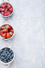 Summer fruit background, top view of berries inside ceramic colored cocotte, blueberries, strawberries, raspberries, flat lay, gray table. Detox and healthy food concept. Copy space.