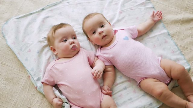 girls twin sisters in pink clothes lying on the bed