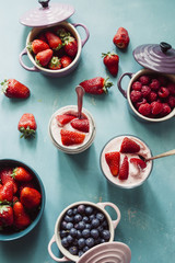 Strawberry cheesecake inside glass jar over a blue background and  top view of berries , inside ceramic colored cocotte, blueberries, strawberries, raspberries, flat lay