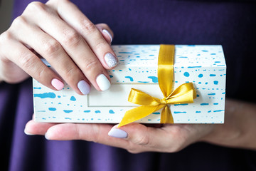 Present box with a gold bow with macaroons inside. Woman holds a box with biscuits.