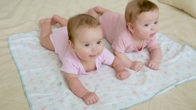 girls twin sisters in pink clothes lying on the bed