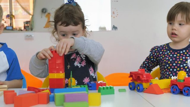 Children's developing a game room. Emotions of young children during entertaining classes. Boys and girls are playing with wooden blocks sitting at the table.