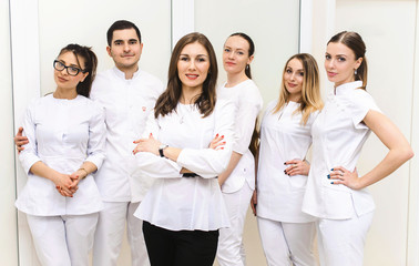 Obraz premium Cheerful group of young dentists and their assistants standing in the dental office and looking at camera and friendly smiling at white background of medical room.