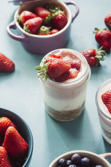 Strawberry cheesecake inside glass jar over a blue background and  top view of berries , inside ceramic colored cocotte, blueberries, strawberries, raspberries, flat lay