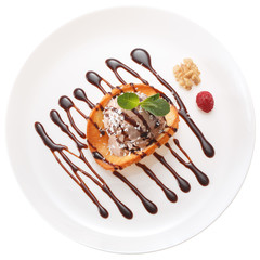 Chocolate ice cream ball decorated with chocolate syrup, nuts, raspberries, mint leaves and coconut chips on a wafer of coconut and honey. All on white plate isolated on white background.