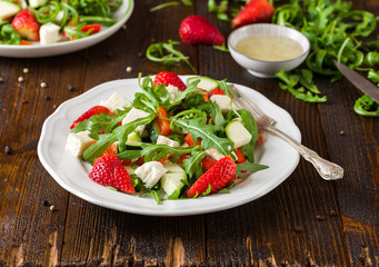 Fresh vegetable strawberry salad on white plate on natural rustic desk.