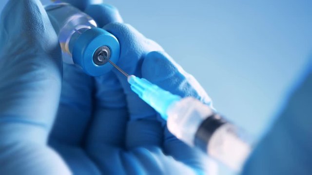 Doctor in blue latex gloves fill in syringe with medicine from glass vial