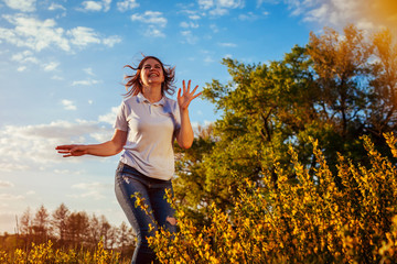 Young woman jumping, running and having fun in spring field at sunset. Happy and free girl relaxes and enjoys nature