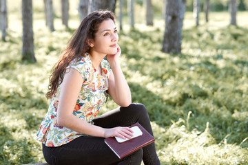 happy young girl sitting on a log in the forest, bright sunlight around, beauty of nature in spring