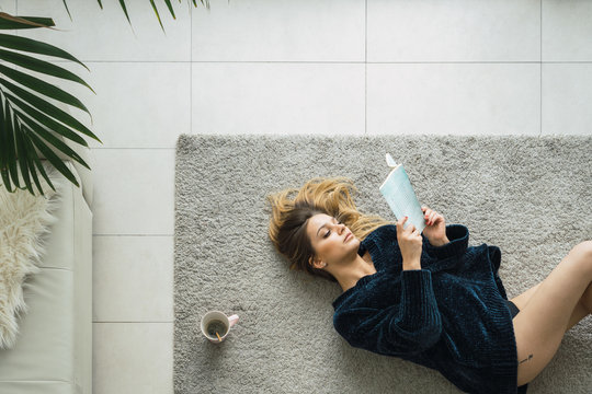 Woman with coffee and book on carpet