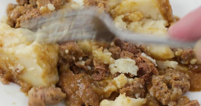 Close video of a meatloaf with mashed potatoes and gravy TV dinner on a white plate being mashed with a fork.