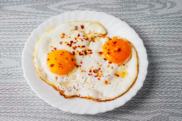 Fried eggs on a plate with chili peper.