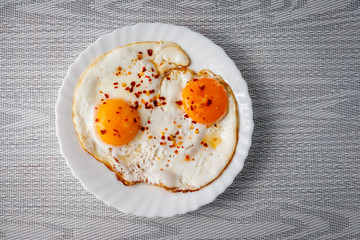 Fried eggs on a plate with chili peper.