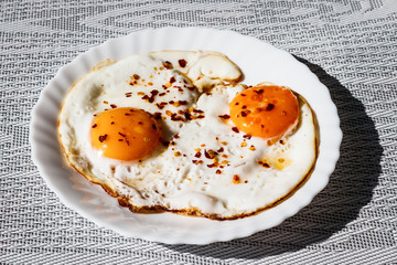 Fried eggs on a plate with chili peper.