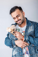 man in denim jacket holds pomeranian dog.