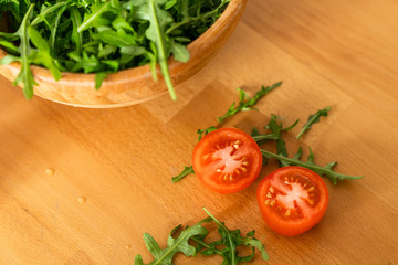 Wooden Bowl of fresh green, natural arugula with cherry tomatoes on a wooden table