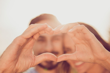 Close up cropped photo of two relaxed carefree cute sweet gentle tender lovely beautiful nice pretty handsome lovers making showing heart people are on blurred background selective focus