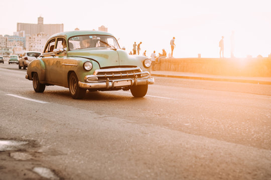 Fototapeta Vintage car driving down road in sunset