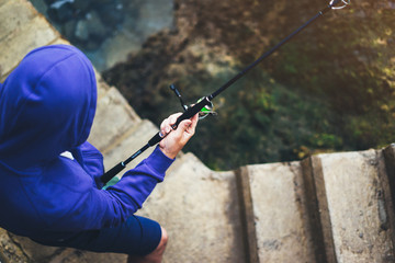 young man holds a fishing rod and catches fish in the nature on a sea background, hipster fisherman spends vacation on the blue ocean, active travel hobby fishing, rural outdoor sport tourism