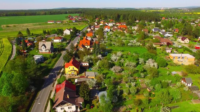 Camera flight over area for pleasant living in suburban district. Houses in beautiful gardens with blooming trees. Beautiful spring nature on Czech countryside. European landscape from above. 