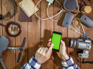 phone with chroma key in the person hands on a wooden surface with gadgets