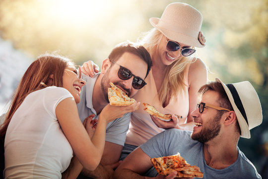 Close up of four young cheerful people eating pizza