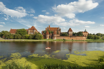 Naklejka na ściany i meble Marlbork castle in northern Poland/largest castle in the world built by the Teutonic knights in the thirteenth century seen across a pond where tourist ride a hydro bicycle.