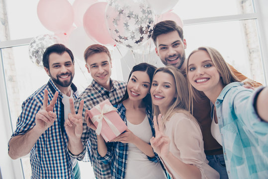 Creative, stylish, attractive, cheerful business people having air balloons cases in package with bow shooting self portrait on front camera showing peace symbol two fingers celebrating event