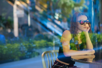 Young woman wearing sunglasses looking out reflected blue and green glass