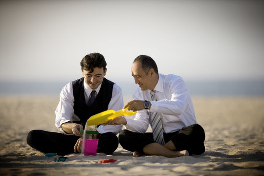 Two businessmen enjoy themselves as they play with the sand on the beach.