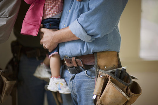 Mid section of a man wearing a tool belt carrying his daughter