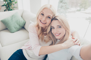 Self portrait of pretty charming attractive mother and daughter bonding shooting selfie on front camera sitting on couch in living room enjoying free time indoor in comfortable cozy atmosphere