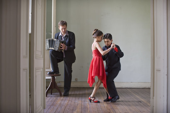 Boy and girl dancing in room while young man plays accordion