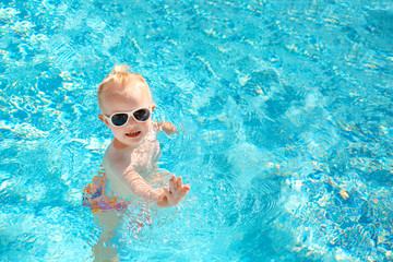 Fototapeta na wymiar Cute baby splashing in the pool in the summer. Top view. Copy space.