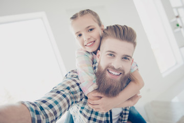 Self portrait of cheerful stylish father with red hair carrying on back cute little schoolgirl,...