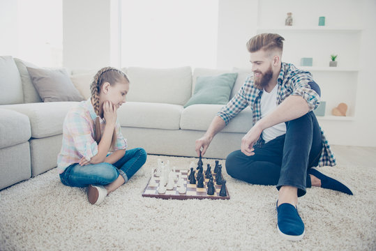 Portrait of family with one parent, stylish trendy kid and daddy playing chess moving figures sitting on carpet near sofa in modern livingroom indoor, style, lifestyle, hairstyle, casual outfit