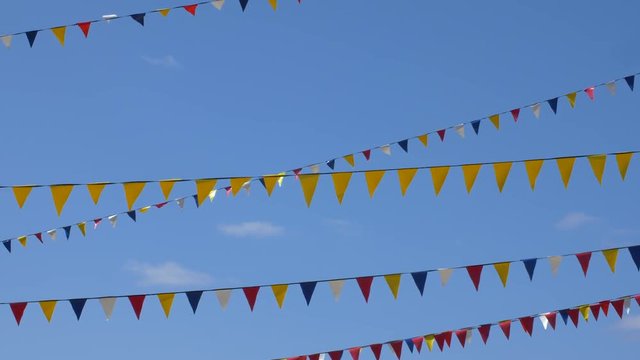 Yellow, blue, white and red triangle flags for carnival party on sky background. Seamless loop background.
