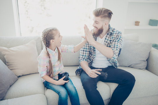 Good job my best friend! Cheerful joyful positive stylish family with one parent, dad giving high five to daughter after victory in car racing game on x-box sitting indoor on couch in livingroom