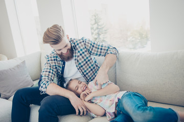 Fototapeta premium Family with one parent, stylish father with good humor kidding with excited laughing daughter on sofa in living room happy moments dreamday funny game babysitting