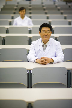Portrait of male teacher in lab coat sitting in lecture hall
