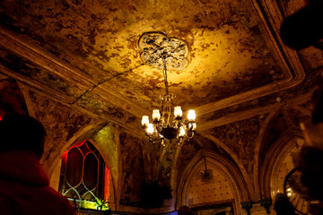 The old chandelier hangs in an old room with a dirty ceiling.