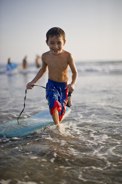 Portrait of smiling boy running in sea with surfboard